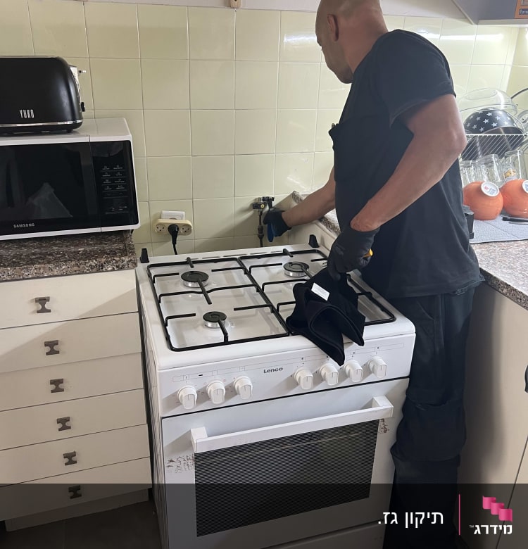 אדם מתקין כיריים גז במטבח עם כפפות עבודה